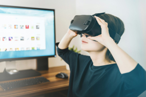 Frau mit VR-Brille vor Computerbildschirm, probiert Extended Reality aus.